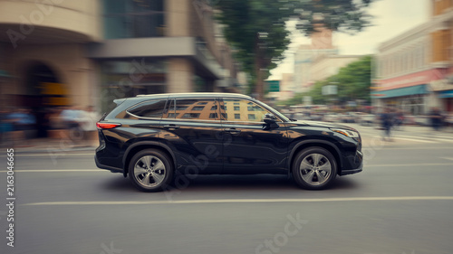 Black SUV driving on a city street with motion blur effect Keywords: car, SUV, black, vehicle, driving, street, city, urban, motion blur, speed, movement