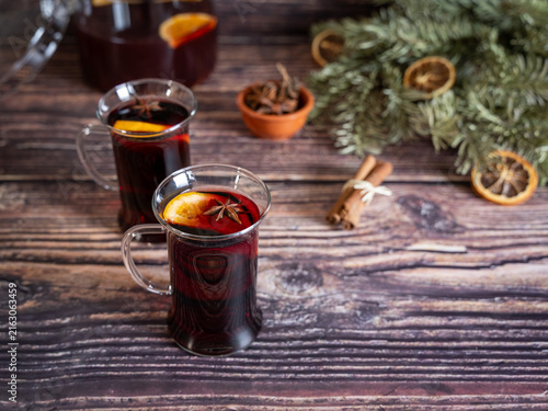 Fotografía Two glasses of warm mulled wine arranged on a rustic wooden table with cinnamon sticks dried orange slices and evergreen Christmas decorations