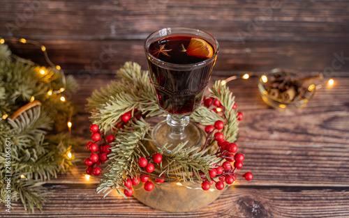 Canvastavla Festive glass of warm mulled wine surrounded by evergreen branches red berries dried orange slices and glowing Christmas lights on a rustic wooden table