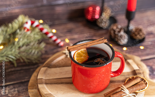Canvastavla Warm mulled wine served in a red enamel mug on a wooden serving board with cinnamon sticks dried orange evergreen branches and festive Christmas decorations