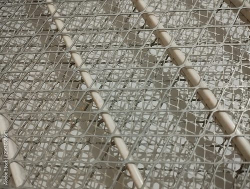 Close-up view of a white mosquito repellent coil protected by a metal wire mesh, creating an intricate geometric pattern. The image represents mosquito prevention, insect protection, pest control