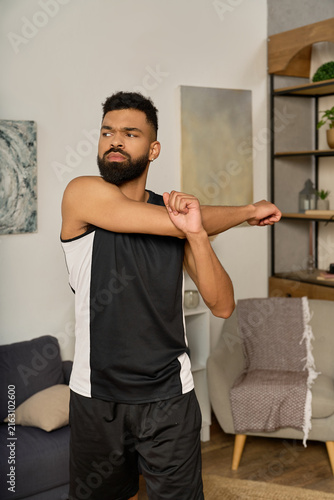 A young, handsome African American man stretches his arm at home, enjoying a relaxing moment.