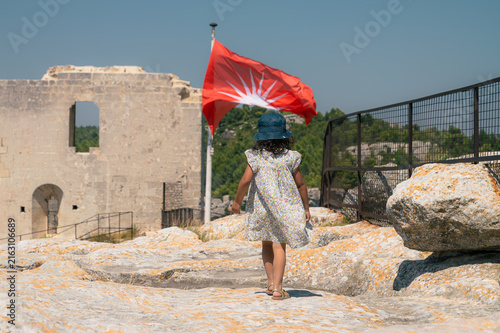 Photography Fillette au chapeau marchant vers un drapeau au château des Baux-de-Provence