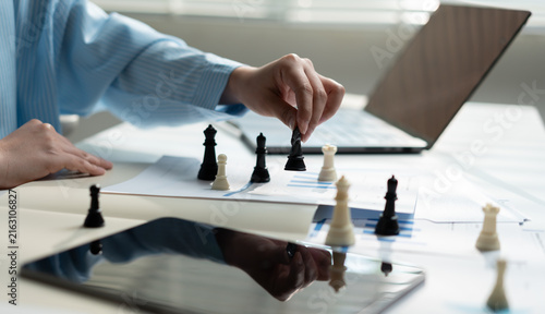 Business professional moving a chess piece over financial reports at an office desk, symbolizing strategic planning, leadership, competition, decision making, risk management and business growth.