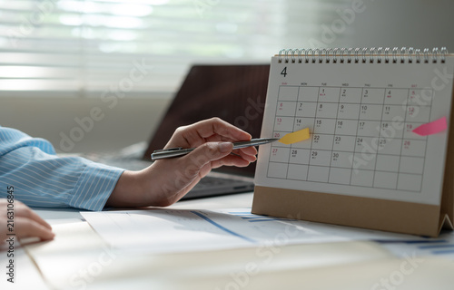 Business professional marking a desk calendar while reviewing reports, representing schedule planning, deadline management, appointment organization, productivity, project timing and office workflow.