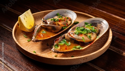 two hot plates of grilled scabbard clams are presented on a wooden grill the clams are covered in a savory sauce and garnished with green onions