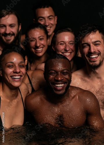 Group photo of a group of six people, all of whom are smiling and looking at the camera. they are in a pool of water, with their bodies partially submerged in the water.