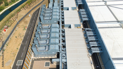 Aerial view of a hyperscale data center featuring rows of industrial air handling units and chillers on the roof, adjacent to a paved road and a canal in Hereford, England, United Kingdom.
