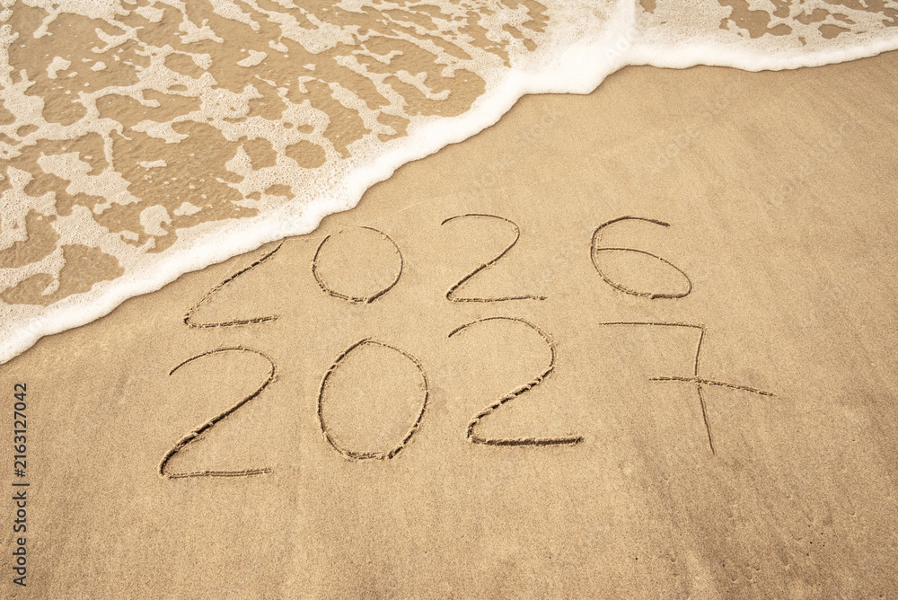 Fototapeta premium Inscription 2026 and 2027 numbers written on sand. New Year 2026 replace 2027. Concept on the sea beach