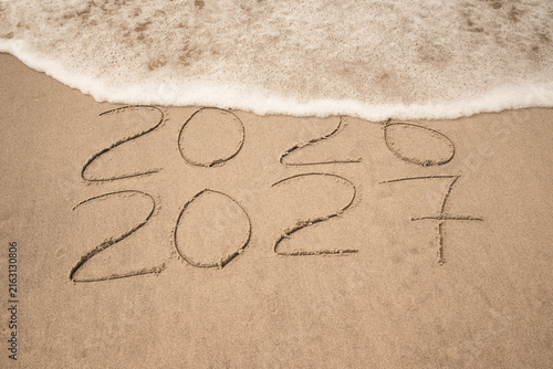 Inscription 2026 and 2027 numbers written on sand.  New Year 2026 replace 2027. Concept on the sea beach