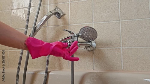 A hand in a bright pink rubber glove works on the chrome shower mixer to eliminate limescale; the image highlights the interaction with the plumbing fixture during the descaling process in a beige-til
