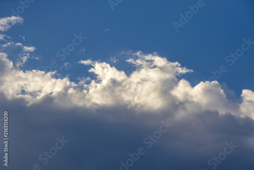 Fotografie Bright blue sky framed by soft white clouds above and dense dark cumulus clouds below