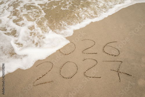 Inscription 2026 and 2027 numbers written on sand.  New Year 2026 replace 2027. Concept on the sea beach