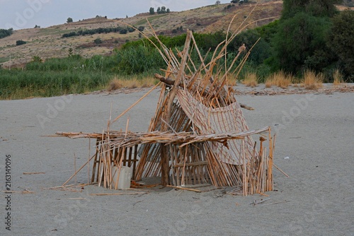 Foto A hut and shelter made of bamboo poles, wooden branches, and fabric on a sandy sea beach
