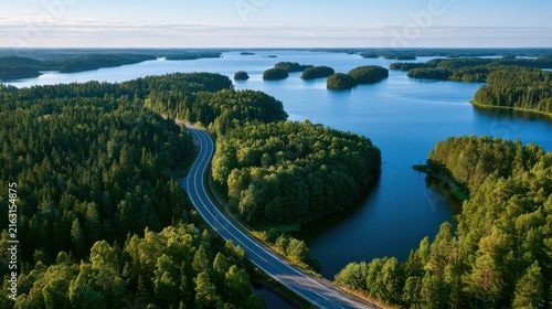 Aerial view of a winding road through lush green forests and blue lakes in Finland. Perfect for travel, transportation, and nature landscape marketing projects.