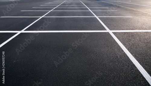 aerial view of empty parking lot with white painted lines on dark asphalt ground surface pattern