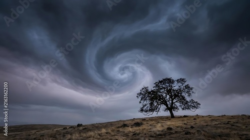 Oak tree on hill under dramatic swirling storm cloud.