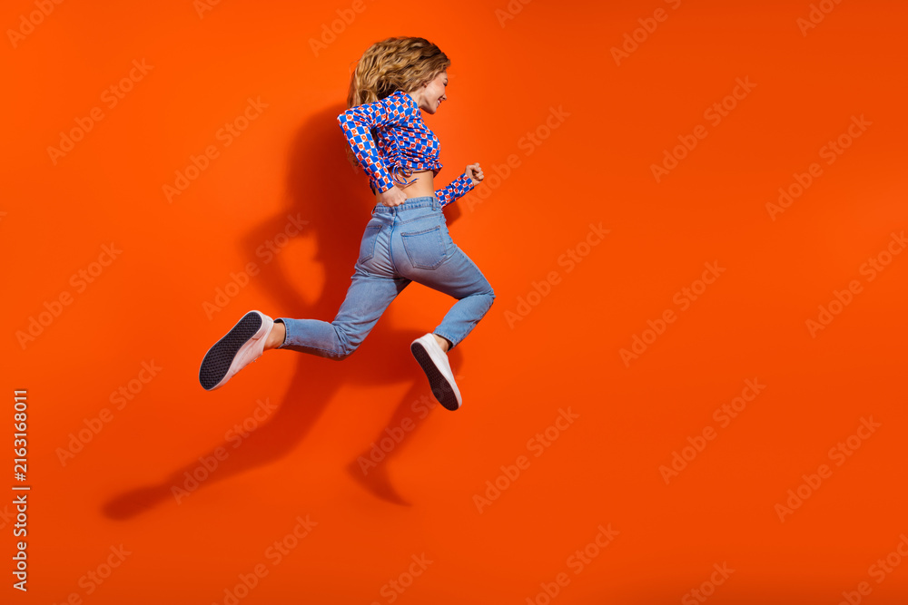 Fototapeta premium Energetic young woman in casual wear jumping joyfully against a vibrant orange background showcasing modern style