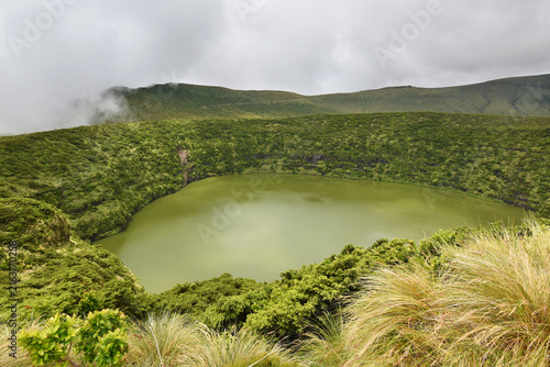 Volcanic crater, Lake Negra surrounded by green vegetation on Flores Island, rain clouds, Azores
