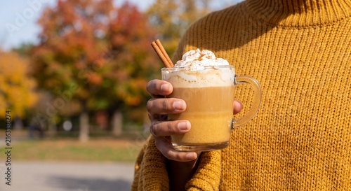 Woman holding pumpkin spice latte with whipped cream outdoors during autumn park foliage