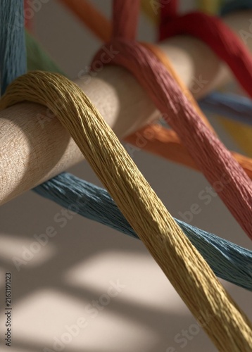 Close-up of a wooden dowel with multiple strands of colorful threads wrapped around it. the threads are of different colors, including red, orange, yellow, green, blue, and purple.