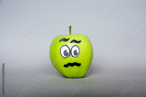 Quadro su tela Funny green apple  Face  character with confused  expression on grey background