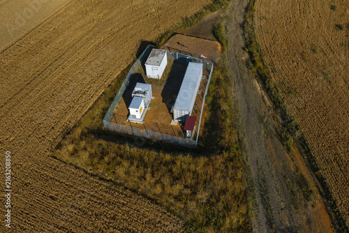 Aerial view of a battery storage facility with industrial containers and electrical equipment enclosed by a fence in a rural field in Uckermark, Brandenburg, Germany.