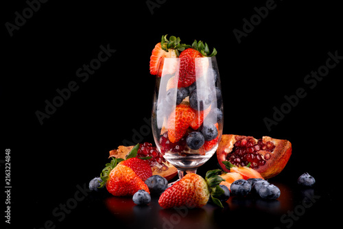 Studio shot of a crystal glass with fresh red berries inside and around it, set against a black background.