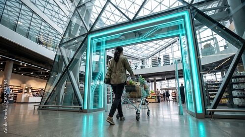 Woman Pushing Shopping Cart Through Futuristic Neon Automated Gate in Modern Supermarket