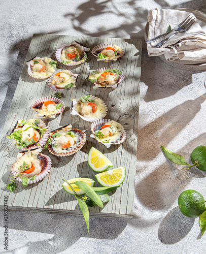 Baked scallops in shells with melted cheese and fresh lime on wooden board