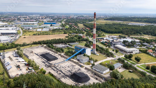 Aerial view of the industrial power plant featuring a tall red and white chimney, coal storage piles, and surrounding buildings in Tczew, Poland.