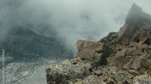 Dramatic mountain summit with jagged rocks lone hiker silhouetted against misty sky. Soft diffused lighting, muted earth tones, moody atmosphere. Ideal for adventure, solitude, nature themes
