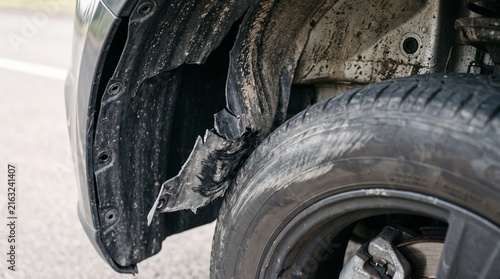 Damaged inner fender liner torn and rubbing against the tire of a modern vehicle on the road. Automotive plastic splash guard broken showing mud, dirt and scrape marks.