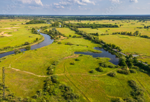 Aerial view of Nadwarcianski Park Krajobrazowy featuring the winding Warta River, lush green meadows, and small ponds under a blue sky in Lad, Greater Poland Voivodeship, Poland.