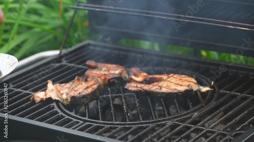 Four fresh salmon fillets cooking on a hot outdoor barbecue grill with smoke rising, preparing a healthy and delicious meal in a backyard setting ideal for summer gatherings