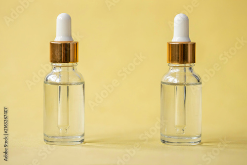 Two cosmetic dropper bottles with clear liquid serum on yellow background