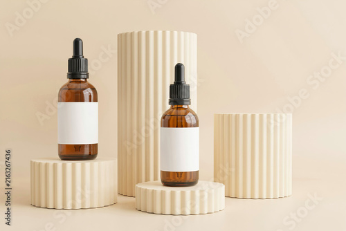 Cosmetic amber glass dropper bottles displayed on beige podiums with cosmetic