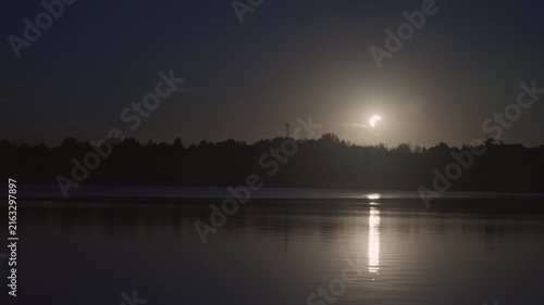 Solar eclipse over lake in timelapse at dusk