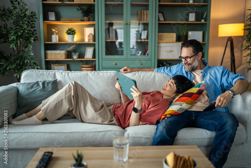 Diverse couple relaxing on sofa using digital tablet together