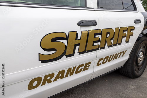 Side view close up of a white Orange County Sheriff patrol car featuring prominent gold and black law enforcement markings across the doors with distinctive American police vehicle styling