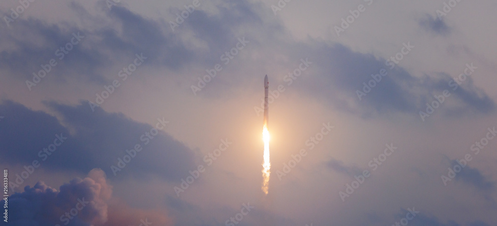 Fototapeta premium Rocket launching into cloudy sky at dusk with dramatic light. Banner of industry technology launching satellites into space