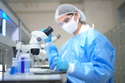 Scientist in protective gear meticulously examines sample under microscope in laboratory setting