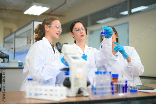 Three female scientists in lab coats and safety goggles collaborating on an experiment