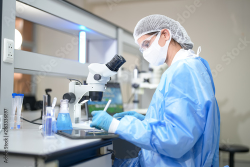 Cuadro en lienzo Scientist in protective gear examining samples under a microscope in a modern la