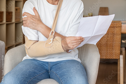 Person wearing an arm sling for a shoulder injury, holding a document representing medical leave, sick leave, or an insurance claim, indicating a period of recovery and healthcare concerns