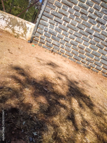 Obraz na płótnie Gray brick wall stands beside a patch of dry brown grass with prominent shadows