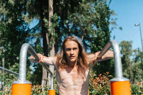 Foto Young athletic man performing dips on outdoor parallel bars
