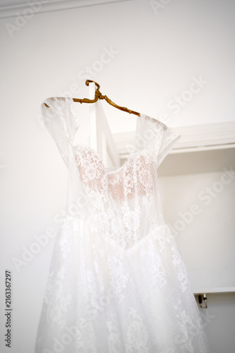 Foto A white lace wedding dress hangs on a wooden hanger in a bright interior before the wedding ceremony