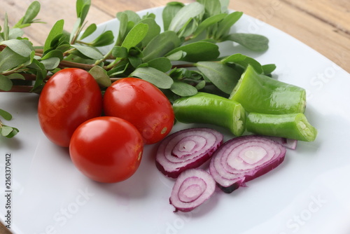 Fresh Purslane Salad Ingredients with Tomatoes, Peppers, and Red Onion Slices on White Plate