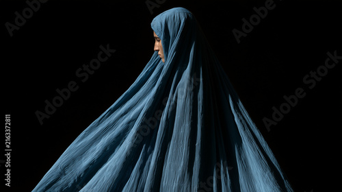 Woman wearing a traditional blue burqa standing against a dark background, symbolizing culture, identity, and the complex layers of tradition and privacy. Afghan culture, burqa por
